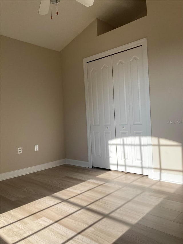 unfurnished bedroom featuring ceiling fan, a closet, light hardwood / wood-style floors, and vaulted ceiling