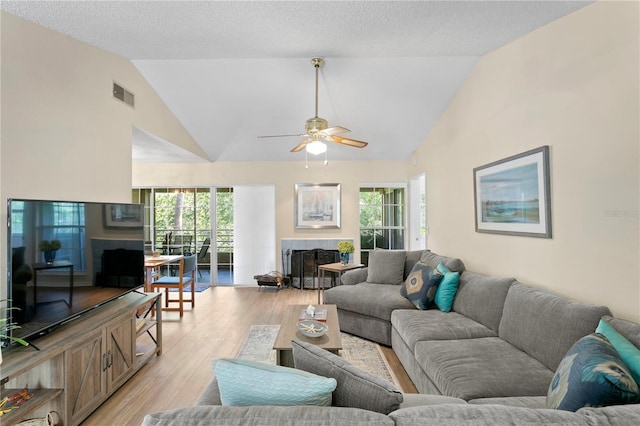 living room featuring light hardwood / wood-style flooring, vaulted ceiling, ceiling fan, a textured ceiling, and a tiled fireplace