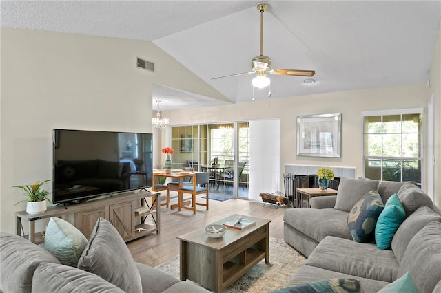 living room featuring a tile fireplace, ceiling fan with notable chandelier, light hardwood / wood-style flooring, and vaulted ceiling