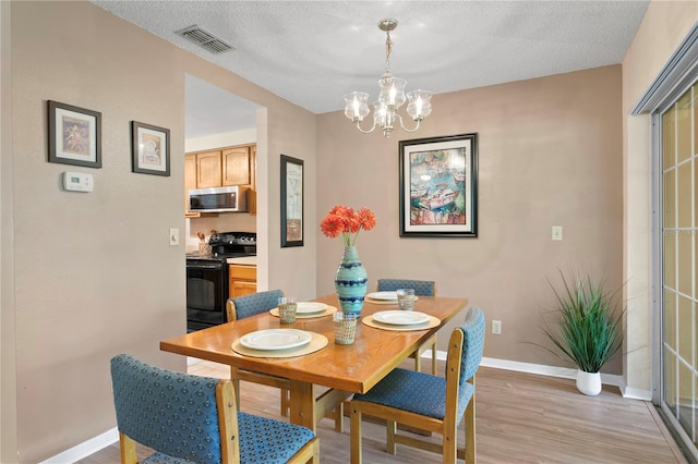 dining area with light hardwood / wood-style flooring, a chandelier, and a textured ceiling