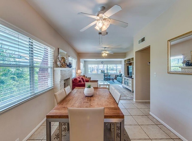 tiled dining room featuring ceiling fan and a fireplace