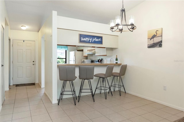 kitchen featuring a kitchen bar, pendant lighting, white refrigerator, a notable chandelier, and white cabinets