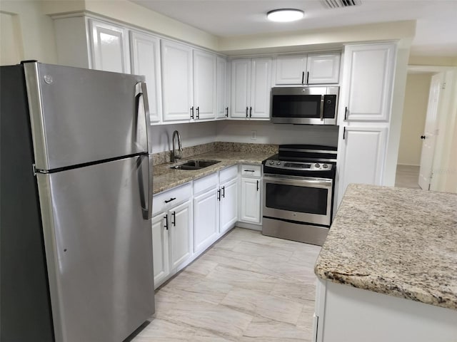 kitchen with sink, stainless steel appliances, white cabinets, and light stone countertops