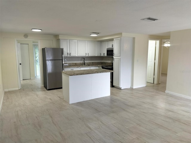 kitchen featuring appliances with stainless steel finishes, sink, dark stone countertops, white cabinets, and a center island