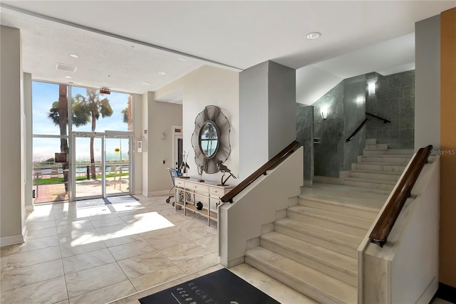 foyer entrance featuring stairway, floor to ceiling windows, visible vents, and baseboards