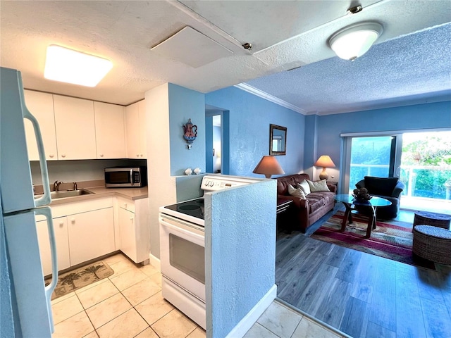 kitchen with white appliances, a textured ceiling, white cabinets, and a sink