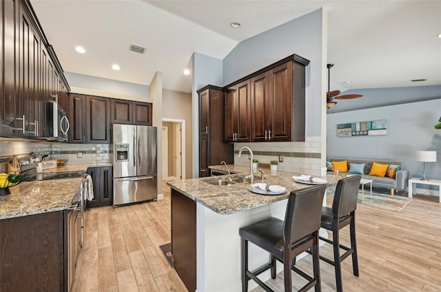 kitchen featuring light stone countertops, backsplash, stainless steel appliances, vaulted ceiling, and sink