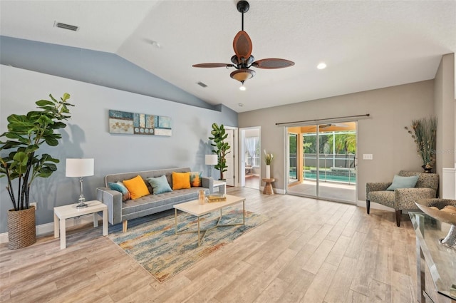 living room with ceiling fan, light wood-type flooring, lofted ceiling, and a textured ceiling