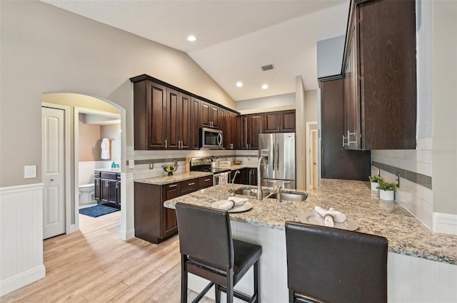 kitchen featuring light stone countertops, appliances with stainless steel finishes, vaulted ceiling, and sink