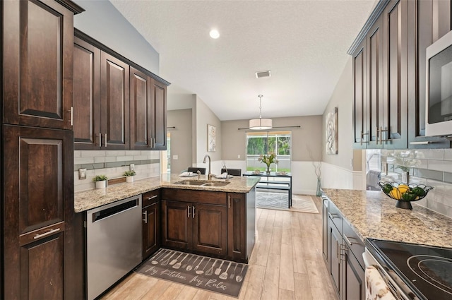 kitchen featuring sink, backsplash, kitchen peninsula, pendant lighting, and appliances with stainless steel finishes