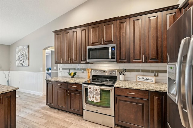 kitchen featuring appliances with stainless steel finishes, tasteful backsplash, light stone counters, and lofted ceiling