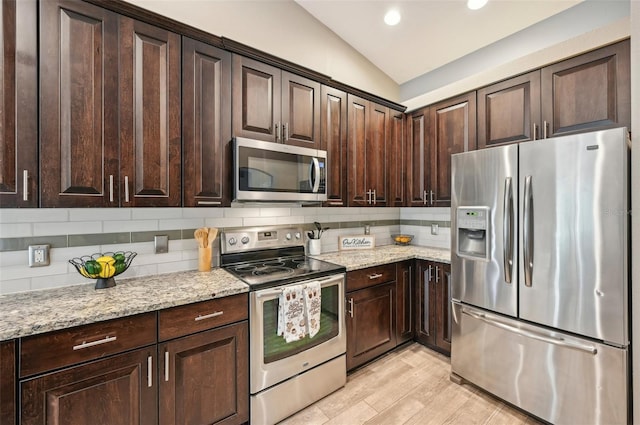 kitchen with stainless steel appliances, tasteful backsplash, light stone counters, vaulted ceiling, and dark brown cabinets