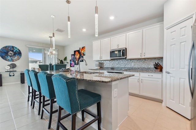 kitchen with a center island with sink, stainless steel appliances, decorative light fixtures, sink, and tasteful backsplash