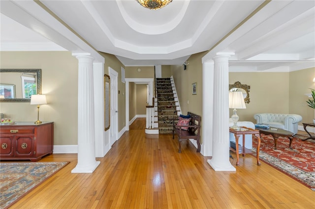 hallway with a tray ceiling, light hardwood / wood-style floors, and ornate columns