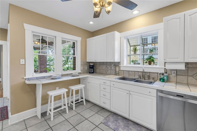 kitchen featuring sink, white cabinetry, stainless steel dishwasher, a healthy amount of sunlight, and backsplash