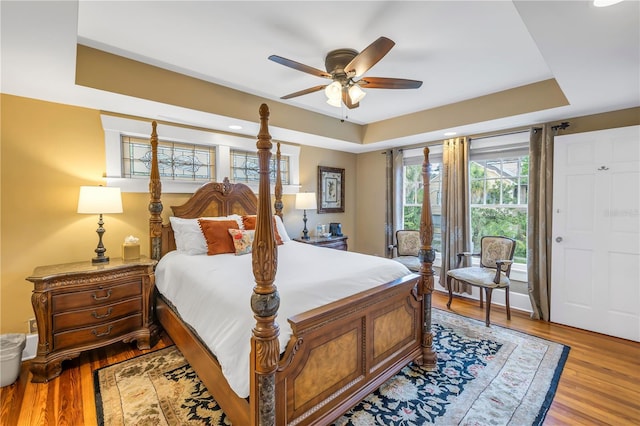 bedroom with a raised ceiling, access to outside, ceiling fan, and light hardwood / wood-style flooring