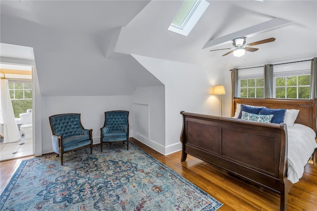 bedroom featuring connected bathroom, hardwood / wood-style flooring, lofted ceiling with skylight, and ceiling fan