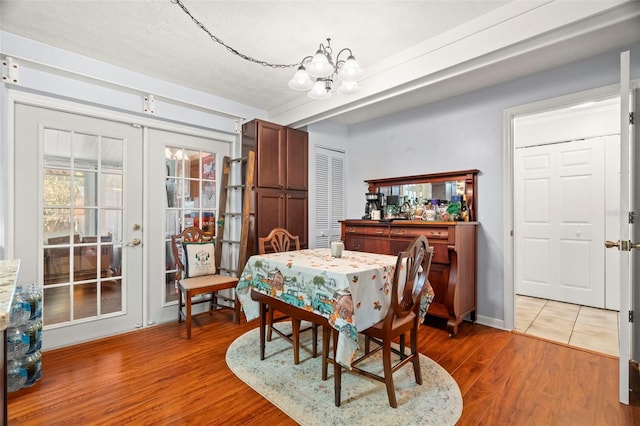 dining area with wood-type flooring, an inviting chandelier, and french doors