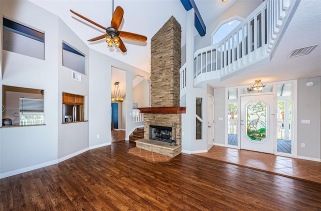 unfurnished living room with wood-type flooring, ceiling fan with notable chandelier, high vaulted ceiling, and a stone fireplace