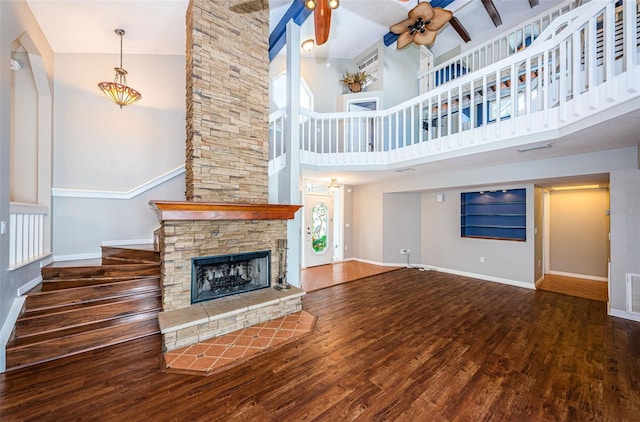 unfurnished living room with ceiling fan, wood-type flooring, beam ceiling, high vaulted ceiling, and a fireplace