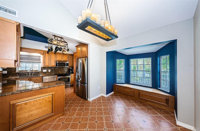 kitchen with dark stone counters, pendant lighting, vaulted ceiling, decorative backsplash, and appliances with stainless steel finishes