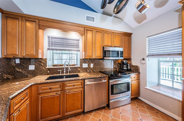 kitchen featuring dark stone countertops, sink, stainless steel appliances, and vaulted ceiling