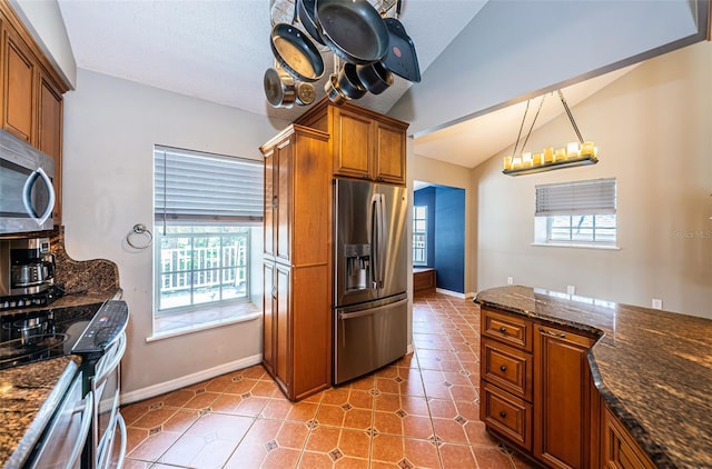 kitchen with tile patterned flooring, dark stone countertops, vaulted ceiling, decorative light fixtures, and appliances with stainless steel finishes