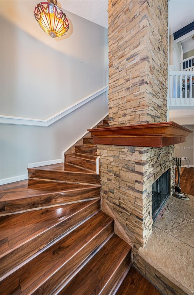 stairway with hardwood / wood-style floors, a textured ceiling, and a stone fireplace