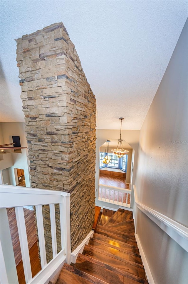 stairs featuring hardwood / wood-style flooring, a textured ceiling, and a chandelier