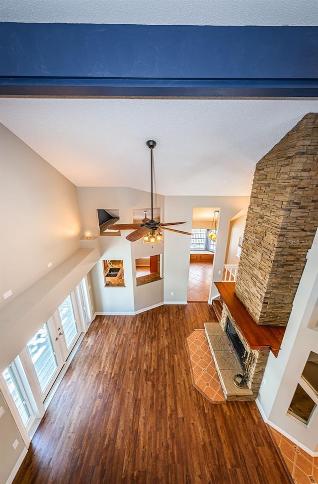 unfurnished living room with plenty of natural light, a stone fireplace, ceiling fan, and dark wood-type flooring