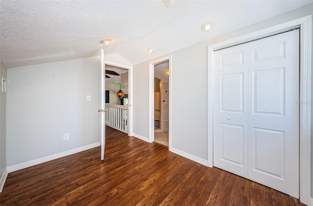 empty room with a textured ceiling, dark hardwood / wood-style flooring, and vaulted ceiling