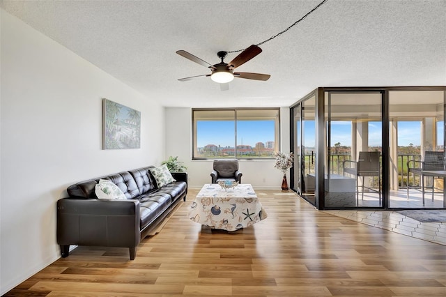 living room with ceiling fan, a textured ceiling, and light wood-type flooring