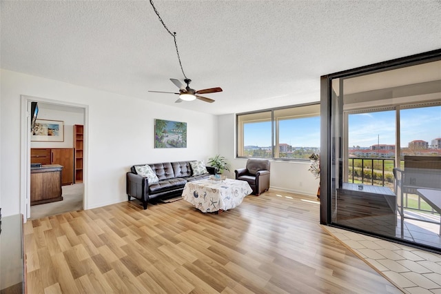 living room with ceiling fan, light hardwood / wood-style flooring, and a textured ceiling