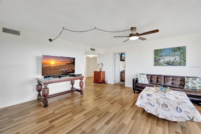 living room with ceiling fan, a textured ceiling, and light wood-type flooring