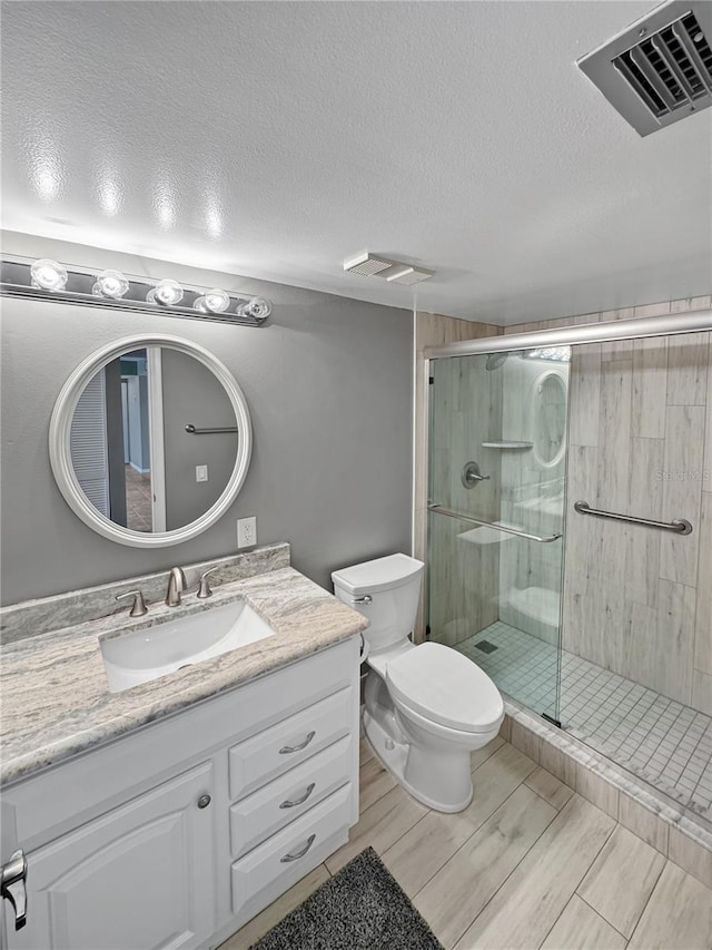 bathroom featuring vanity, a textured ceiling, a shower with door, and toilet