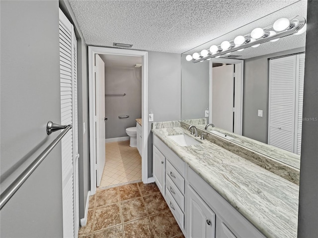 bathroom featuring vanity, toilet, tile patterned flooring, and a textured ceiling