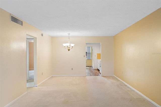 spare room featuring a chandelier and light colored carpet