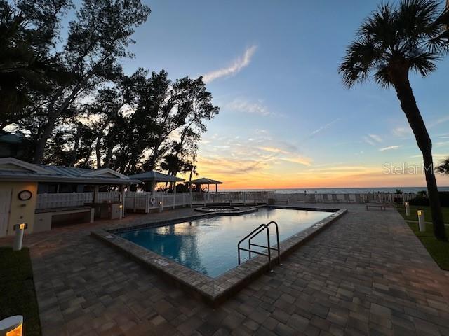 pool at dusk with a patio area and a water view