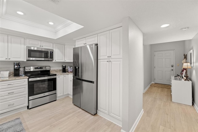 kitchen with white cabinetry, stainless steel appliances, a tray ceiling, and light wood-type flooring