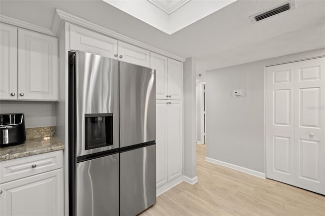 kitchen with white cabinets, stainless steel refrigerator with ice dispenser, light stone counters, and light hardwood / wood-style floors