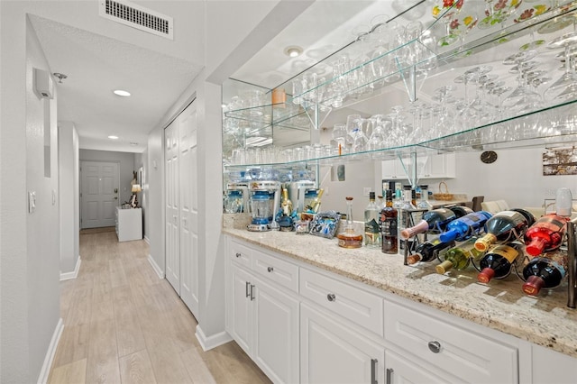 bar featuring white cabinetry, light stone counters, and light hardwood / wood-style flooring