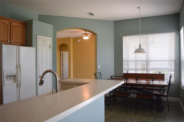 kitchen with dark tile patterned flooring, decorative light fixtures, ceiling fan, and white fridge with ice dispenser