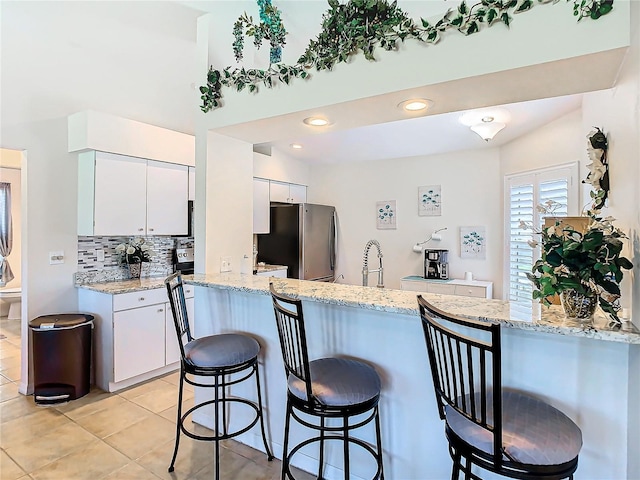 kitchen featuring a breakfast bar, tasteful backsplash, freestanding refrigerator, white cabinetry, and a peninsula