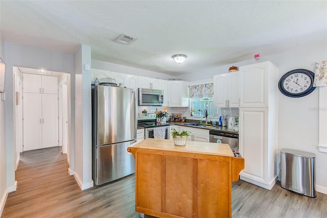 kitchen with decorative backsplash, appliances with stainless steel finishes, sink, light hardwood / wood-style flooring, and white cabinetry