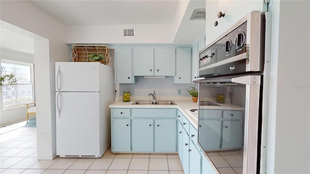 kitchen with sink, backsplash, light tile patterned floors, and white refrigerator