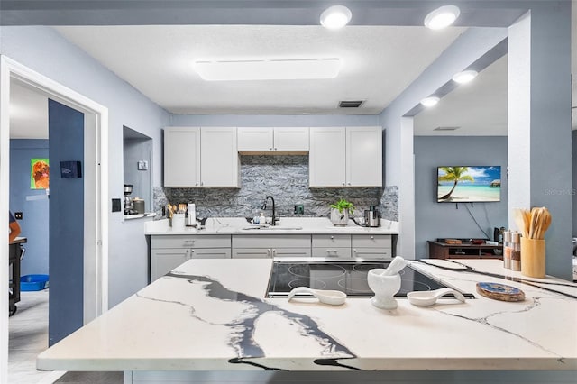 kitchen with stovetop, light stone counters, sink, and tasteful backsplash