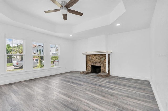 unfurnished living room with a raised ceiling, a fireplace, ceiling fan, and plenty of natural light