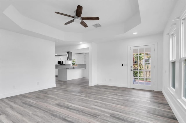 unfurnished living room with light wood-type flooring, a raised ceiling, and ceiling fan