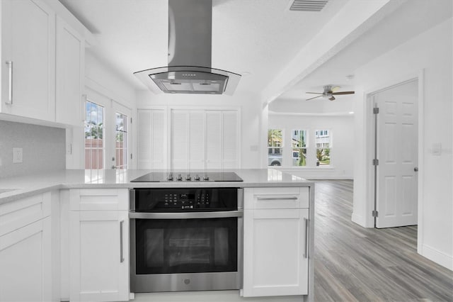 kitchen featuring kitchen peninsula, stainless steel oven, white cabinets, and exhaust hood