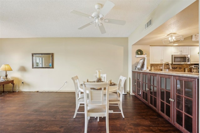 dining space with a textured ceiling, ceiling fan, dark wood-type flooring, and sink